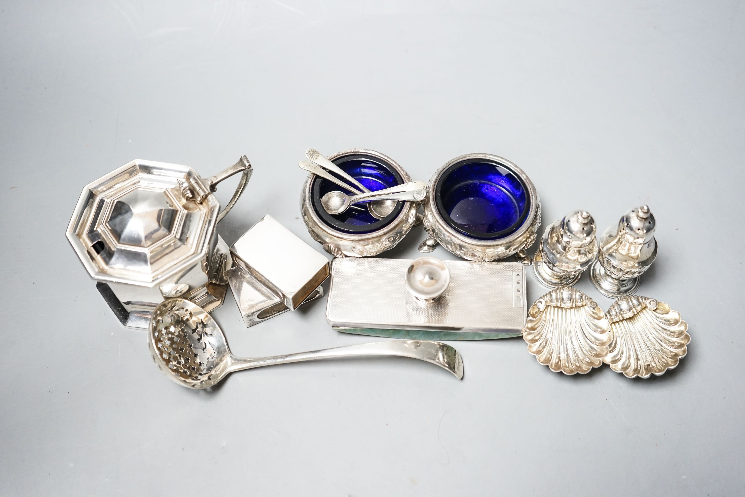 Small silver including a George V silver octagonal mustard, two Victorian bun salts, two shell salts, George III sifter spoon, two condiments, a blotter and two match box sleeves.